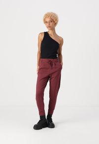 Top in cotone nero a spalla unica abbinato a pantaloni jogger bordeaux con vita con coulisse, gambe affusolate e stivali militari neri.