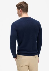 Mörkblå stickad tröja med rund halsringning, långa ärmar och ribbade mudd. Mjuk textur, figurnära design och minimal sömsdetalj.