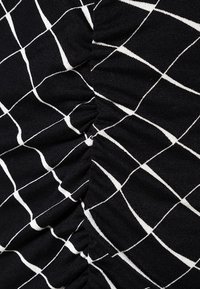 Svart tyg med ett vitt rutmönster, med insnörningar eller rynkor i mitten som framhäver textur och design detaljer.