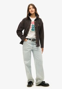 Chaqueta de pana negra con cierre de botones, camiseta gráfica blanca, vaqueros de pierna ancha azul claro, zapatos negros, tejido texturizado, diseño casual.