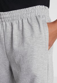 Grå sweatpants med resårmidja, sidofickor och en mjuk, texturerad yta. Tyget verkar vara lätt och bekvämt.