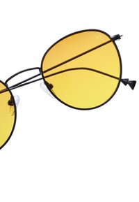 Musta metalliset aurinkolasit, joissa on suuret keltaiset linssit, pyöreä muoto, kaksoissilta-tyyli ja läpinäkyvät nenätyynyt.