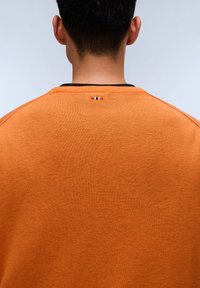 Felpa a maglia arancione con finitura testurizzata. Presenta un colletto nero e un piccolo accento tricolore nella parte posteriore del collo.