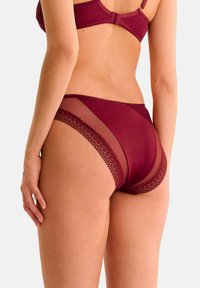 Culotte en dentelle bourgogne avec des panneaux latéraux transparents, un bord en dentelle festonné et une finition en tissu lisse. Conçue pour le confort et l'ajustement.