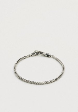 Ασημένιο βραχιόλι από μέταλλο με σχέδιο πλεκτή αλυσίδα, που έχει κούμπωμα και μαύρες λεπτομέρειες κοντά στο κούμπωμα.