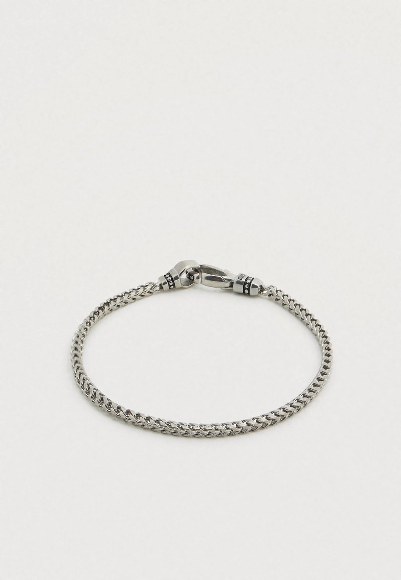 Bracelet en métal argenté avec un design de chaîne torsadée, doté d'une fermeture à boucle et de détails noirs près de la fermeture.