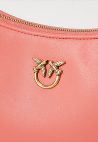 Bolsa de couro coral com um anel dourado e duas ornamentações de pássaros, superfície texturizada e detalhe de zíper dourado na parte superior.
