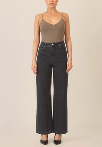 Brauner, enger Body mit dünnen Trägern, kombiniert mit hoch taillierten, dunkelgrauen, weiten Jeans mit Fronttaschen und kontrastierenden Nähten. Schwarze Absatzschuhe.