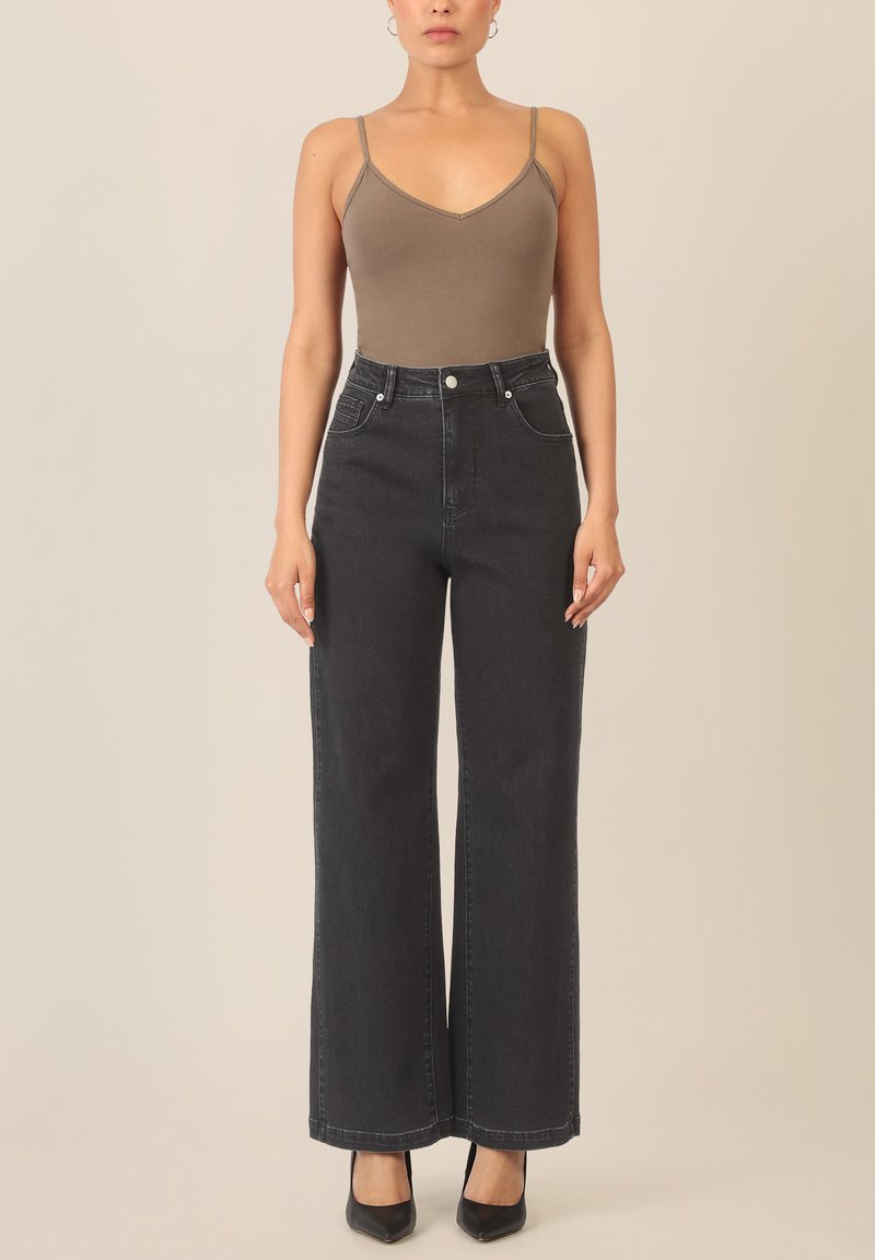 Brauner, enger Body mit dünnen Trägern, kombiniert mit hoch taillierten, dunkelgrauen, weiten Jeans mit Fronttaschen und kontrastierenden Nähten. Schwarze Absatzschuhe.