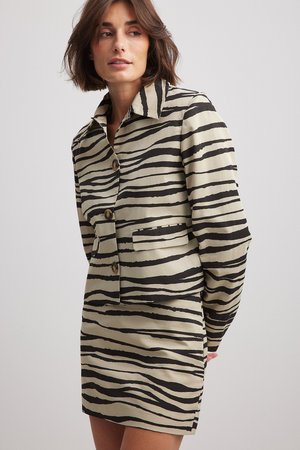 Krémová bunda s čiernymi pruhmi zebra, s golierom, zapínaním na gombíky a prednou vreckom, vyrobená z hladkej látky.