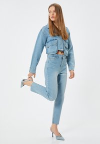 Chaqueta de mezclilla corta color azul claro con bolsillos frontales, combinada con jeans de tiro alto a juego y tacones azules. Textura suave, ajuste casual.