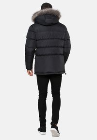 Svart pufferjacka med horisontell quiltning, en foderkrage i päls och elastiska ärmar, tillsammans med svarta tajta byxor och sneakers.