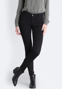 Czarne, wąskie dżinsy wykonane z elastycznego denimu, z średnim stanem, pięcioma kieszeniami oraz gładkim wykończeniem. Noszone z botkami sięgającymi kostki.