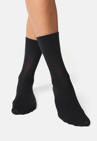 Sorte sokker lavet af et glat strikket materiale, der sidder lige under læggen, med en subtil glans og uden synlige mønstre eller logoer.