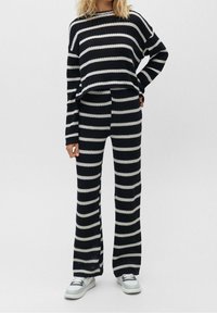 Pull en tricot rayé et pantalon évasé assorti en bleu marine et blanc. Texture douce, coupe ample, motif côtelé, associé à des baskets blanches.