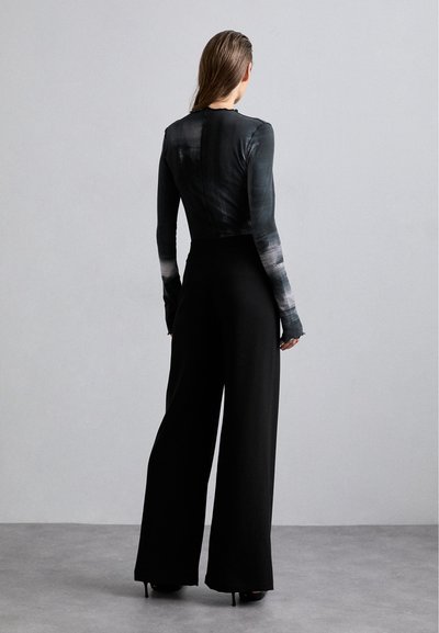 Black wide-leg pants paired with a fitted, gradient black top. Smooth fabric with long sleeves and unique button detailing on the back.