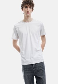 Camiseta blanca de manga corta hecha de algod�ón suave, con un escote redondo y un corte relajado, combinada con jeans gris oscuro.