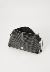 Bolso de cuero negro con forma redondeada, detalles con ojales plateados, cierre de cremallera y un asa metálica en forma de anillo. El interior está forrado en tela.