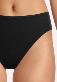 Culotte bikini nera a coste con vita media e texture liscia, progettata per comfort e praticità.