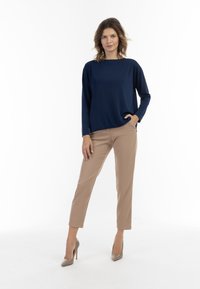 Marineblå langærmet top parret med beige slim-fit bukser og beige højhælede sko, som har en afslappet pasform og glat stofstruktur.