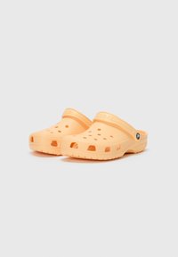 Orange plastic clogs with ventilation holes, adjustable heel strap, and textured sole for grip. Rounded toe and smooth surface finish.