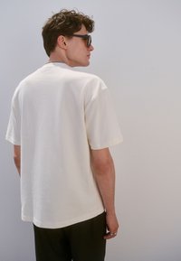 T-shirt beige color crema, dalla vestibilità ampia, realizzata in tessuto morbido, con maniche corte e scollatura arrotondata, con dettagli di cuciture minime sui bordi.