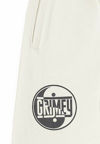 Tela blanca con un logo redondo negro de yin-yang y el texto "GRIMEY" en negrita. El diseño incluye bolsillos laterales para mayor funcionalidad.