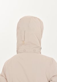 Veste à capuche beige clair avec une texture lisse, dotée d'une fermeture à bouton au niveau du cou et d'une petite boucle en tissu sur la capuche.