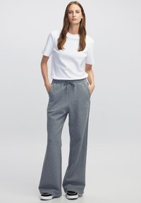 Witte t-shirt met korte mouwen gecombineerd met grijze losse joggingbroeken, voorzien van een elastische tailleband en zijzakken, aangevuld met zwarte sneakers.