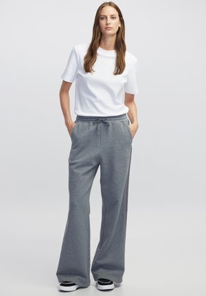Witte t-shirt met korte mouwen gecombineerd met grijze losse joggingbroeken, voorzien van een elastische tailleband en zijzakken, aangevuld met zwarte sneakers.