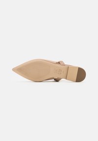 Escarpin beige à bout pointu avec une finition lisse, semelle texturée et un talon bloc bas. Présente un design de bride sur le dessus.