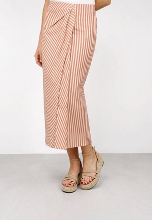 Mujer que lleva una falda midi de rayas verticales rosas y blancas con un delantero drapeado y sandalias beige con plataforma y tiras en el tobillo.