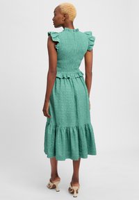 Mintgrünes Kleid mit strukturiertem Stoff, Rüschenschultern, tailliertem Oberteil und gestuftem Rock. Es hat einen hohen Ausschnitt und einen Reißverschluss auf der Rückseite.