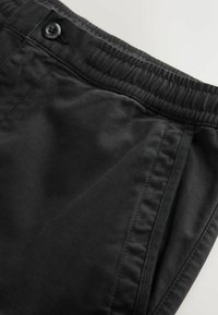Black pants featuring a textured fabric, elastic waistband, button closure, and side pockets, with neat stitching along the edges.