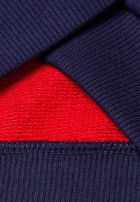 Primer plano de tela azul marino acanalada doblada que revela un forro interior texturizado rojo con costuras detalladas a lo largo del borde.