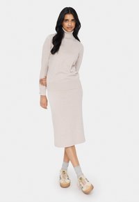 Beige stickad turtleneck-tröja i kombination med en matchande midje-lång kjol, som har en avslappnad passform och mjuk textur. Sneakers i blandade färger.