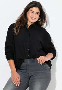 Black long-sleeve button-up shirt made from textured fabric, paired with dark gray fitted jeans, featuring a smooth surface and side pockets.