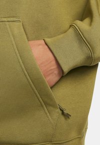 Olijfgroene hoodie met een kangoeroezak, ribbelmanchetten en een getextureerde stof met een ritssluiting aan de zijzak.
