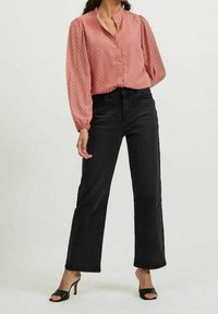 Rosa blus med chevron-mönster, knappframsidan och puffärmar, kombinerad med höga svarta vida jeans och svarta klacksandaler.