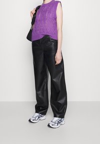 Haut tricoté sans manches violet avec un motif en câble, associé à un pantalon large en similicuir noir et des baskets argentées de style sportif.