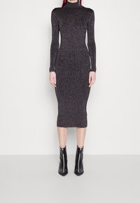 Robe tricotée à manches longues en gris foncé avec un éclat métallique, silhouette ajustée, longueur genoux, associée à des bottines noires à fermeture éclair.