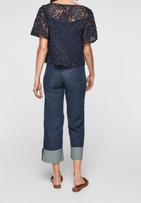Haut en dentelle bleu marine avec des motifs floraux, associé à un pantalon en denim bleu foncé cropped avec des ourlets roulés et des poches arrière.