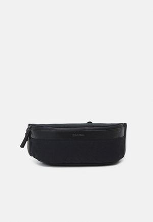 Zwarte Calvin Klein heuptas met voorvak met rits en verstelbare band, ontworpen voor handsfree dragen en casual gebruik.