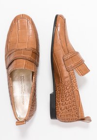 Tan faux leather shoes with a crocodile texture. Slip-on design features a strap and low heel for stability. Smooth interior lining.