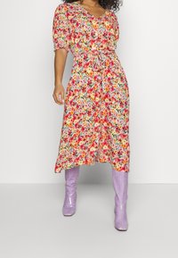 Abito midi floreale in giallo, rosa e verde con maniche a sbuffo, vita cintrata e cintura avvolgente. Abbinato a stivali lavanda fino al ginocchio.