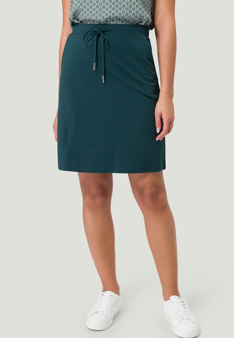 Türkisfarbener Baumwollrock mit Kordelzug an der Taille, knielang und glatter Textur. Kombiniert mit weißen Turnschuhen für einen lässigen Look.