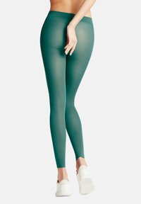 Leggings teal en tissu extensible avec une texture lisse, dotés d'une taille haute et d'une coupe ajustée, associés à des baskets blanches.