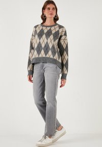 Sivi in bež argyle pleten pulover z ohlapnim fitom, ki ima širok ovratnik in rebraste manšete, v kombinaciji s sivimi jeans hlačami in športnimi copati.