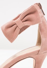 Escarpin en daim rose avec un accent en nœud sur la bride de la cheville, présentant un intérieur lisse et un design de talon effilé.