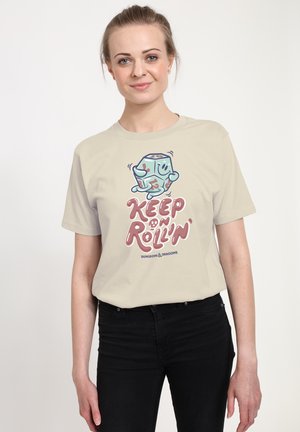 Beige bomulds t-shirt med en tegneserie terning karakter og teksten "Keep on Rollin'" i pink, sammen med sorte jeans. Enkel rund halsudskæring, korte ærmer.